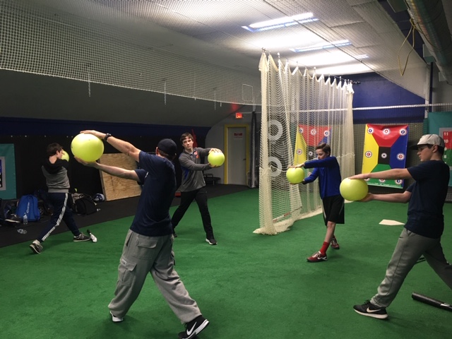 Players swinging at oversized training balls during a hitting drill in the cages